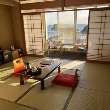Japanese Ryokan hotel with tatami floors low table with two chairs, window with view of the ocean in the background.