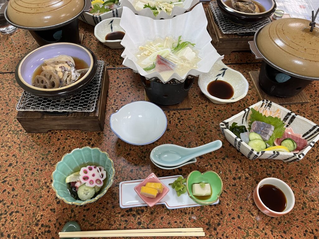 Japanese dinner served at a Ryokan including small dishes of sashimi, fish on a grill, tofu and mushrooms in a hot put and more.