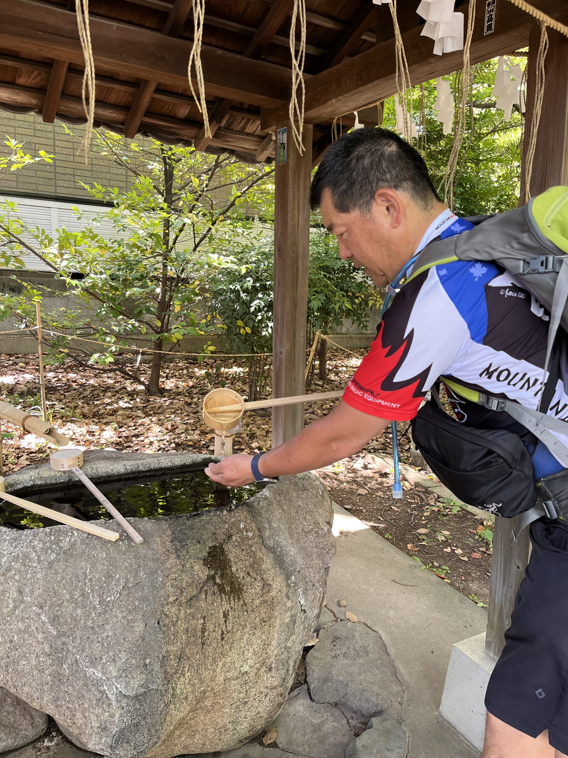 Man washing his hands at a temle with a small cup from a rock basin of water. This practice is known as Temizusha.