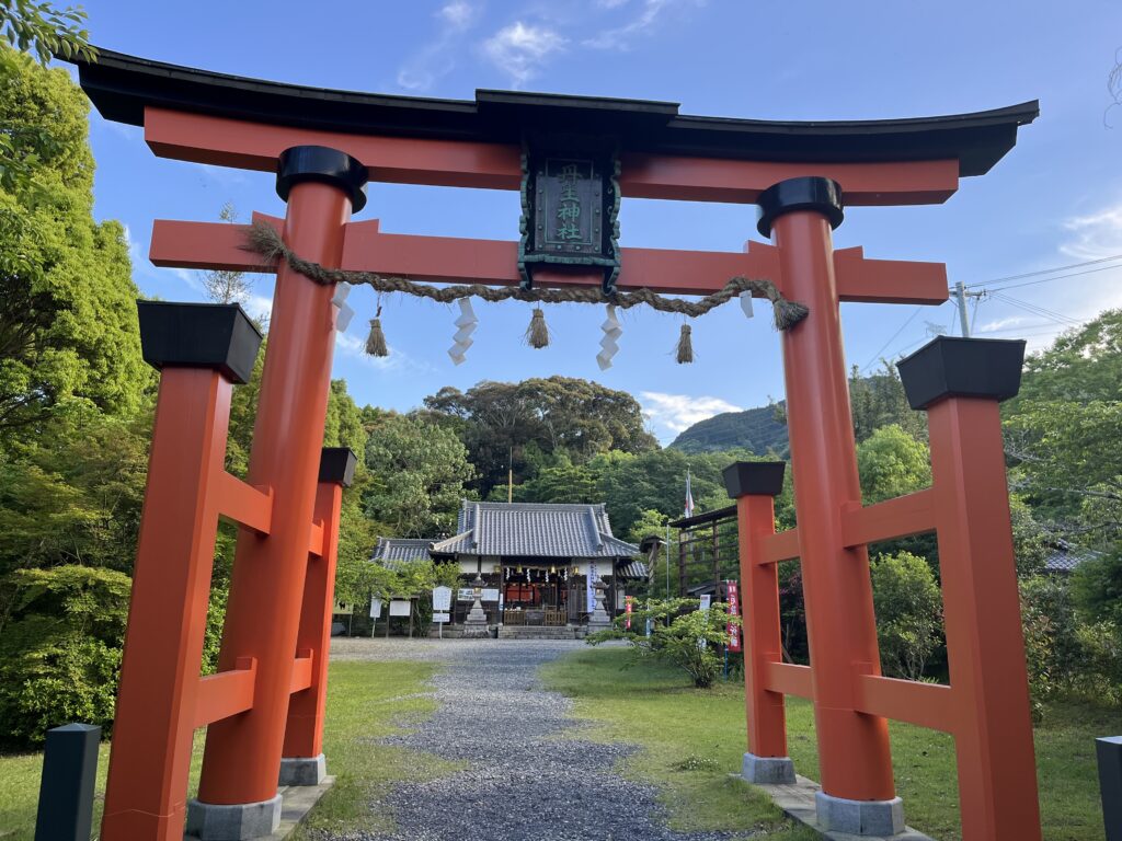 Red and black tori gate marking the entrance to a Shinto shrine in Japan on a blue sky day.