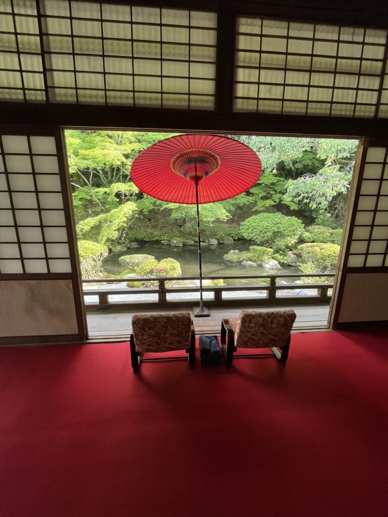 View of two chairs looking onto a Japanese garden with red umbrella. Enman-inn Otsu.