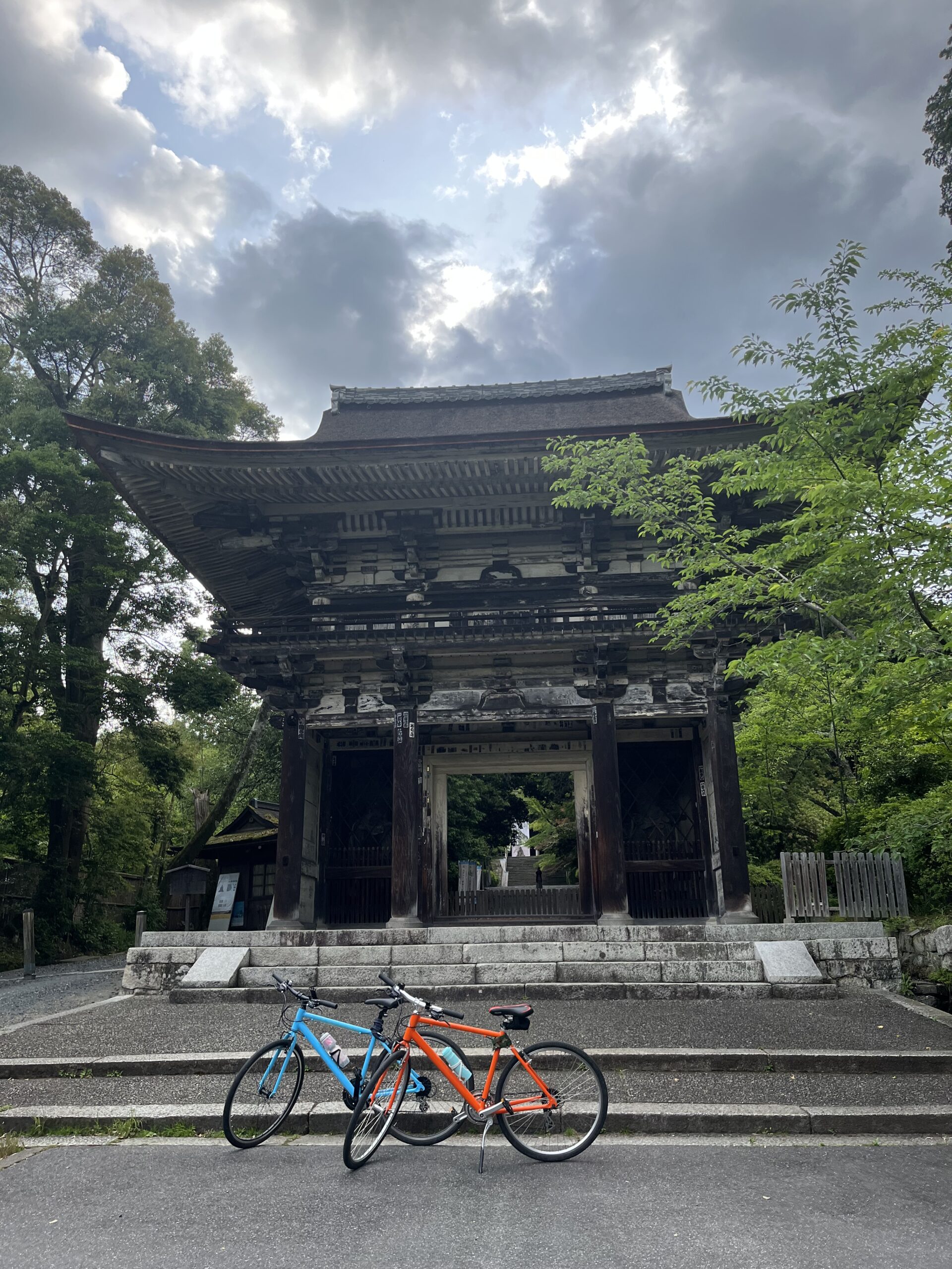 Two bikes, orange and blue parked outside a temple entrance with a cloudy sky in the background.