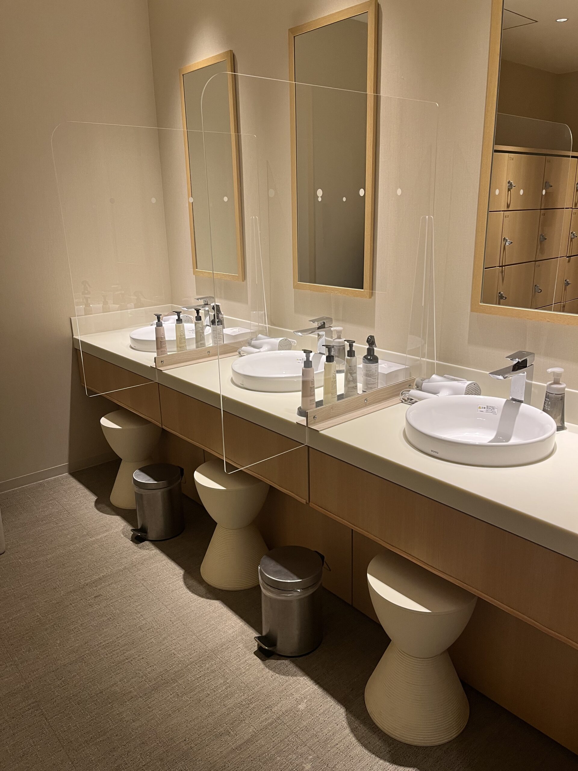 Spa room in Japan with three sinks, three mirrors and small stools tucked under the counter.