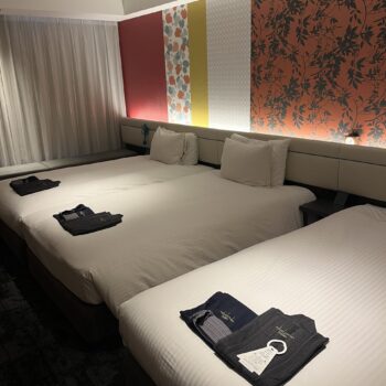 Hotel with three beds and pajamas on the bed with bright colored wall paper on the wall.