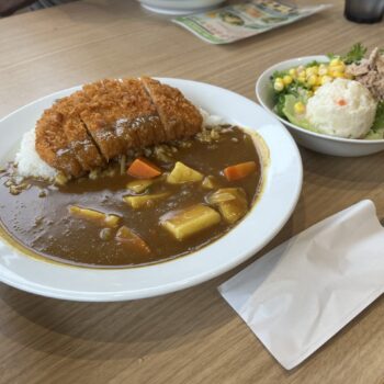 Katsu curry, Japanese curry with potatoes and carrots on a bed of rice, served with a breaded and deep fried cutlet and a side salad with tuna and potato salad on a bed of lettuce with corn.