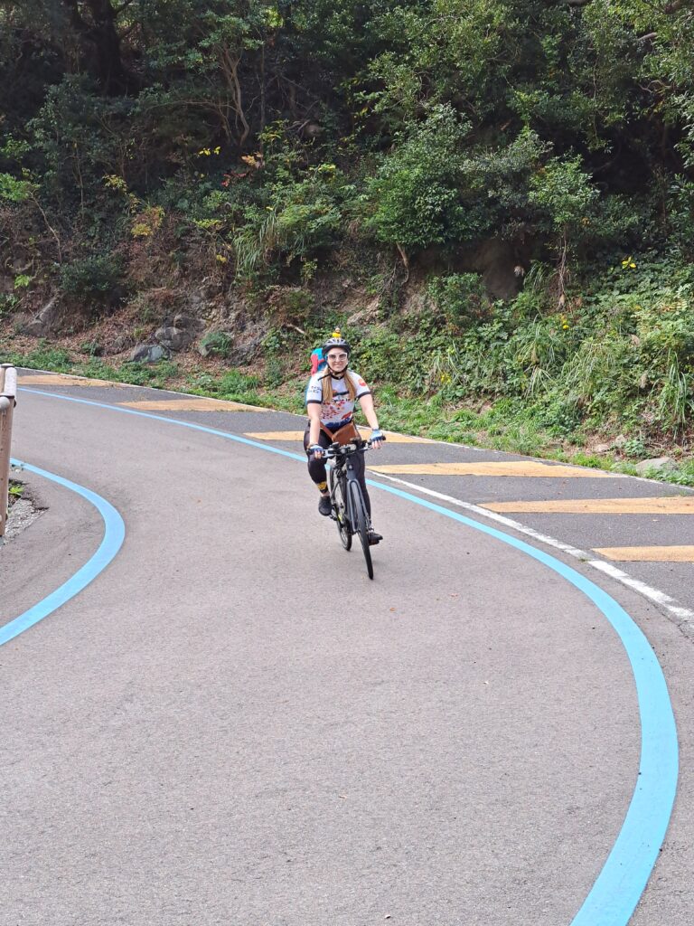 A smiling cyclist coming downhill on a paved road with blue bike lines on the path.