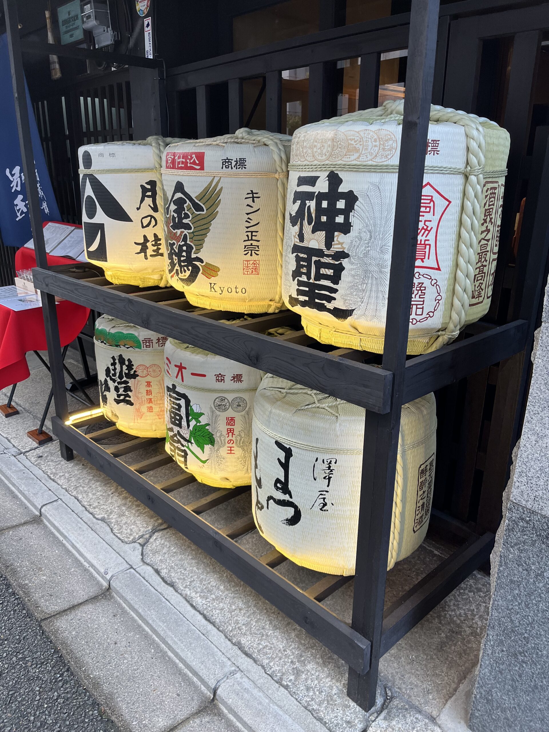 Sake barrels with three on top shelf and three on the bottom shelf in front of a restaurant in Kyoto.
