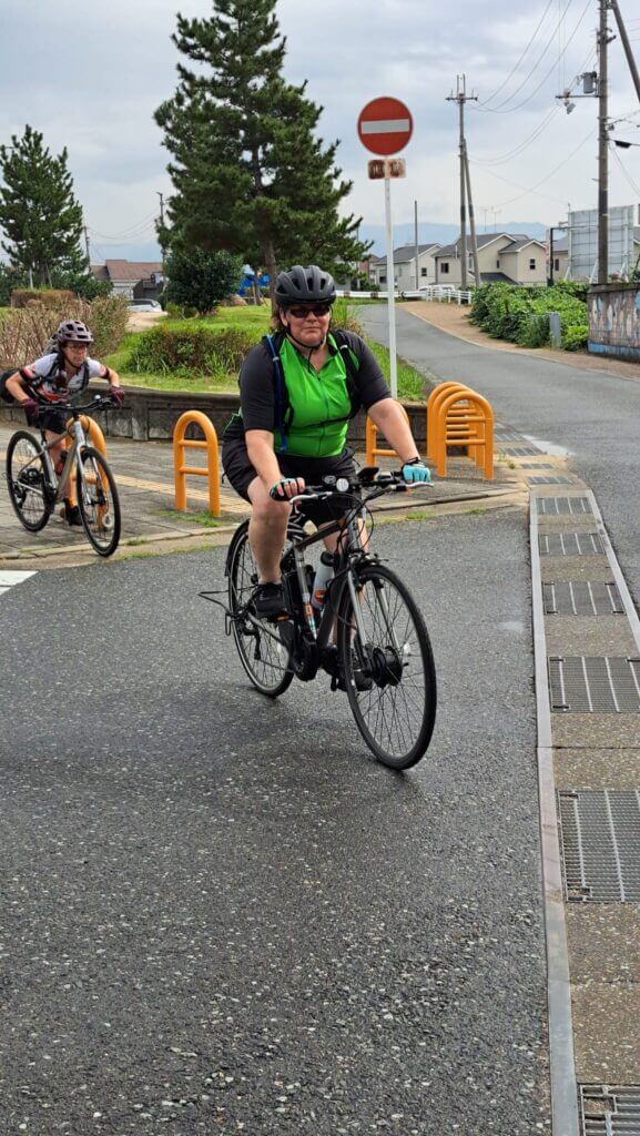 Woman in green and black jersey cyclists on a road.