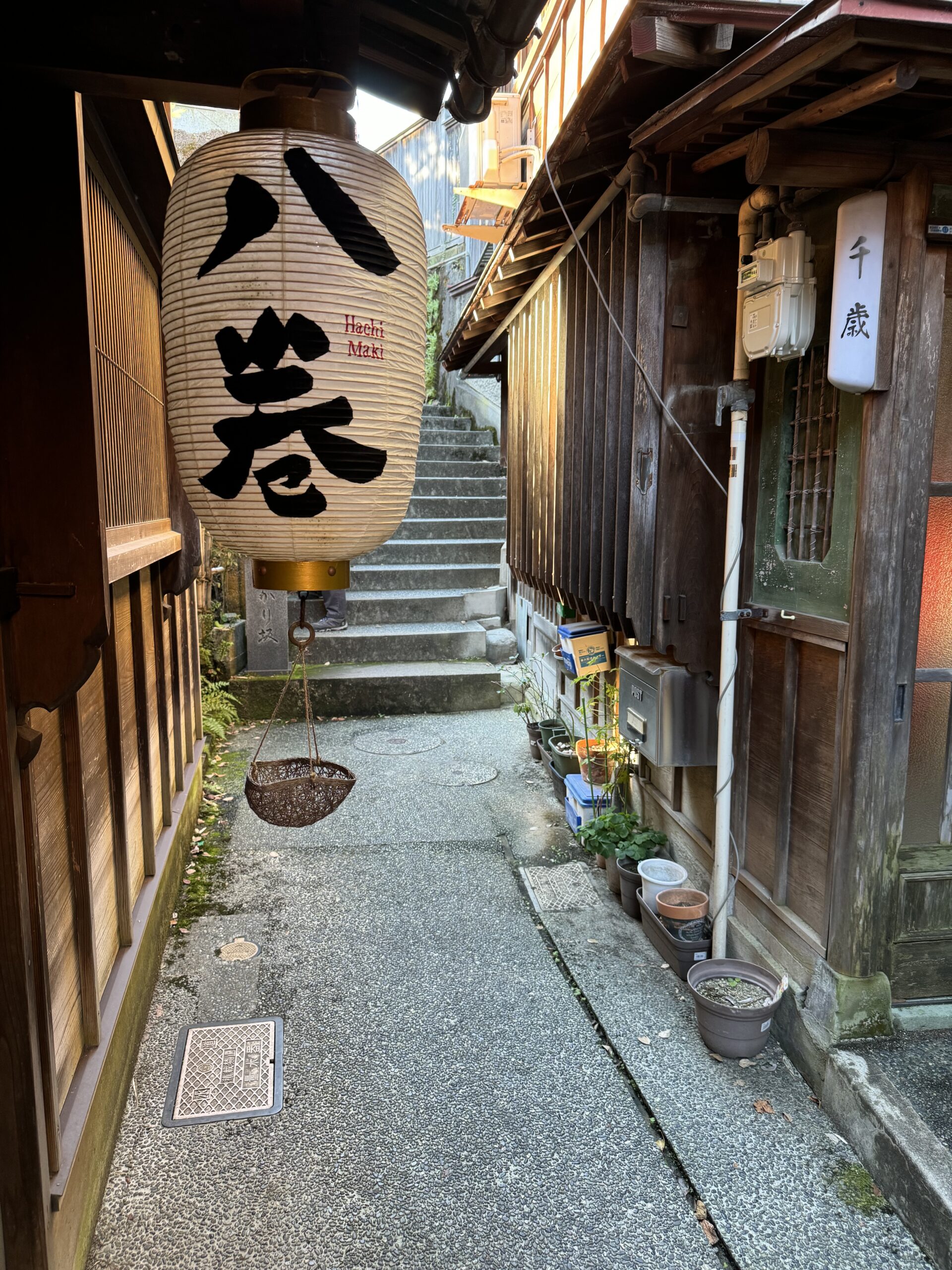 White paper lantern hangs from storefront on narrow street with stairs in background in a Chaya neighborhood in Kanazawa.