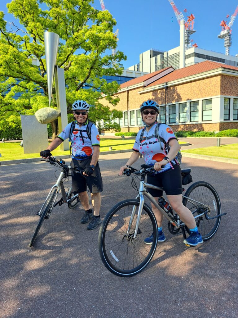 Two cyclists stop outside Panasonic Museum with big smiles.