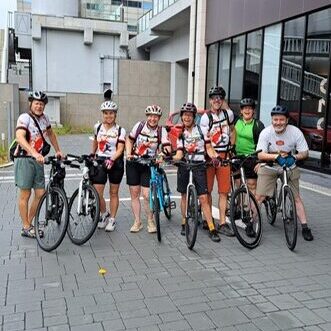 Group of seven cyclists pose with their bikes in front of a building.