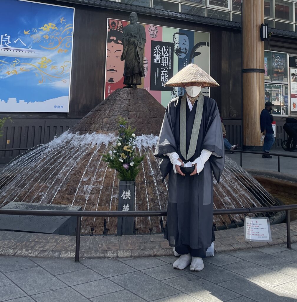 Buddhist monk stands outside statue in Nara collecting donations.
