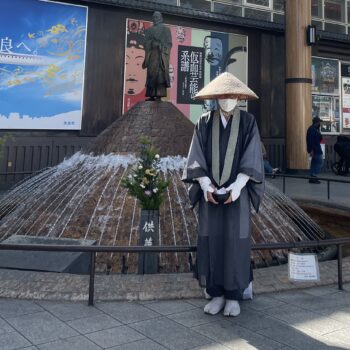 Buddhist monk stands outside statue in Nara collecting donations.