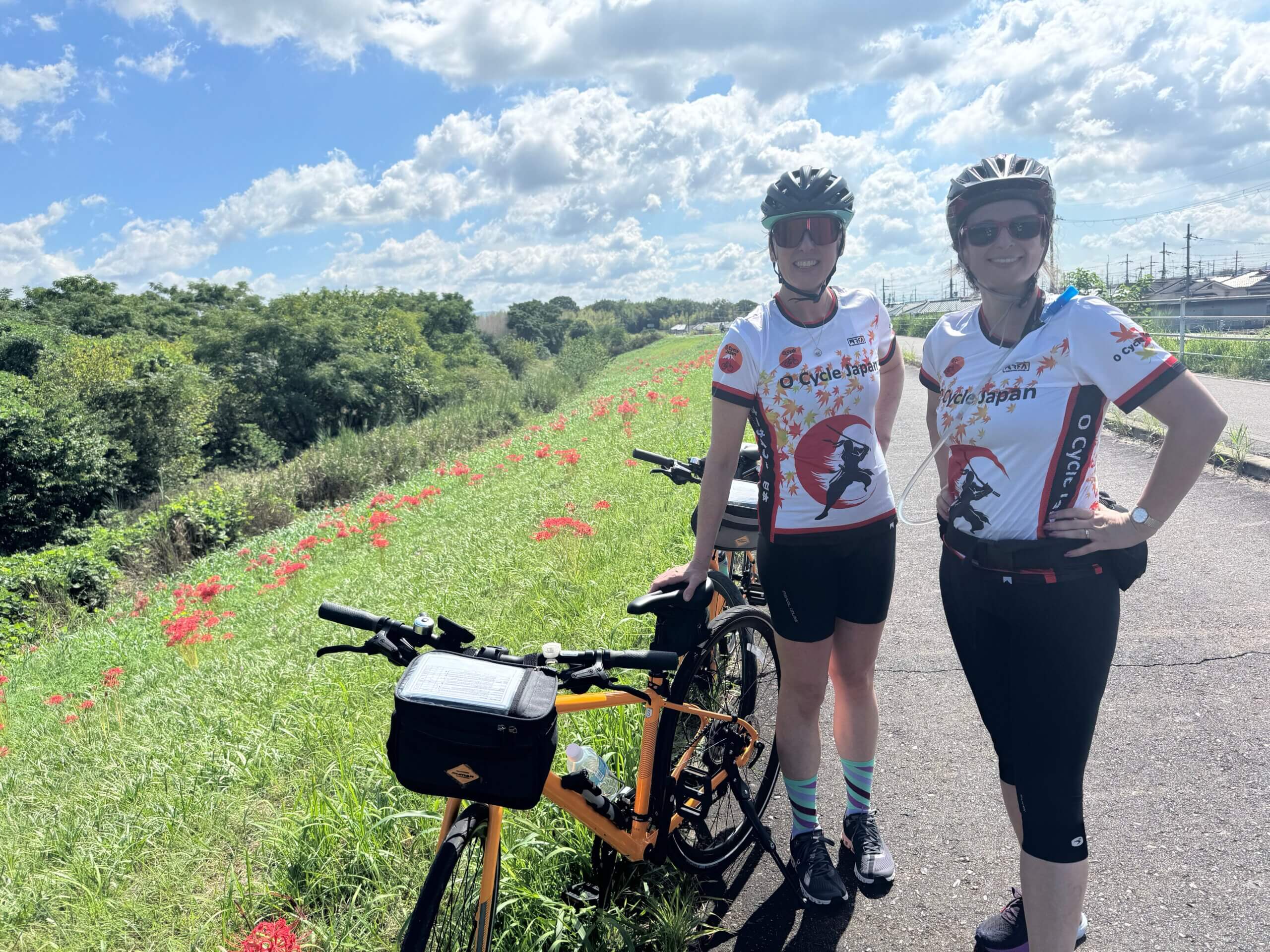 Two women in O Cycle Japan cycling jersey's stop to admire the fall Spider Lily flowers in Japan while cycling in the Kansai region.
